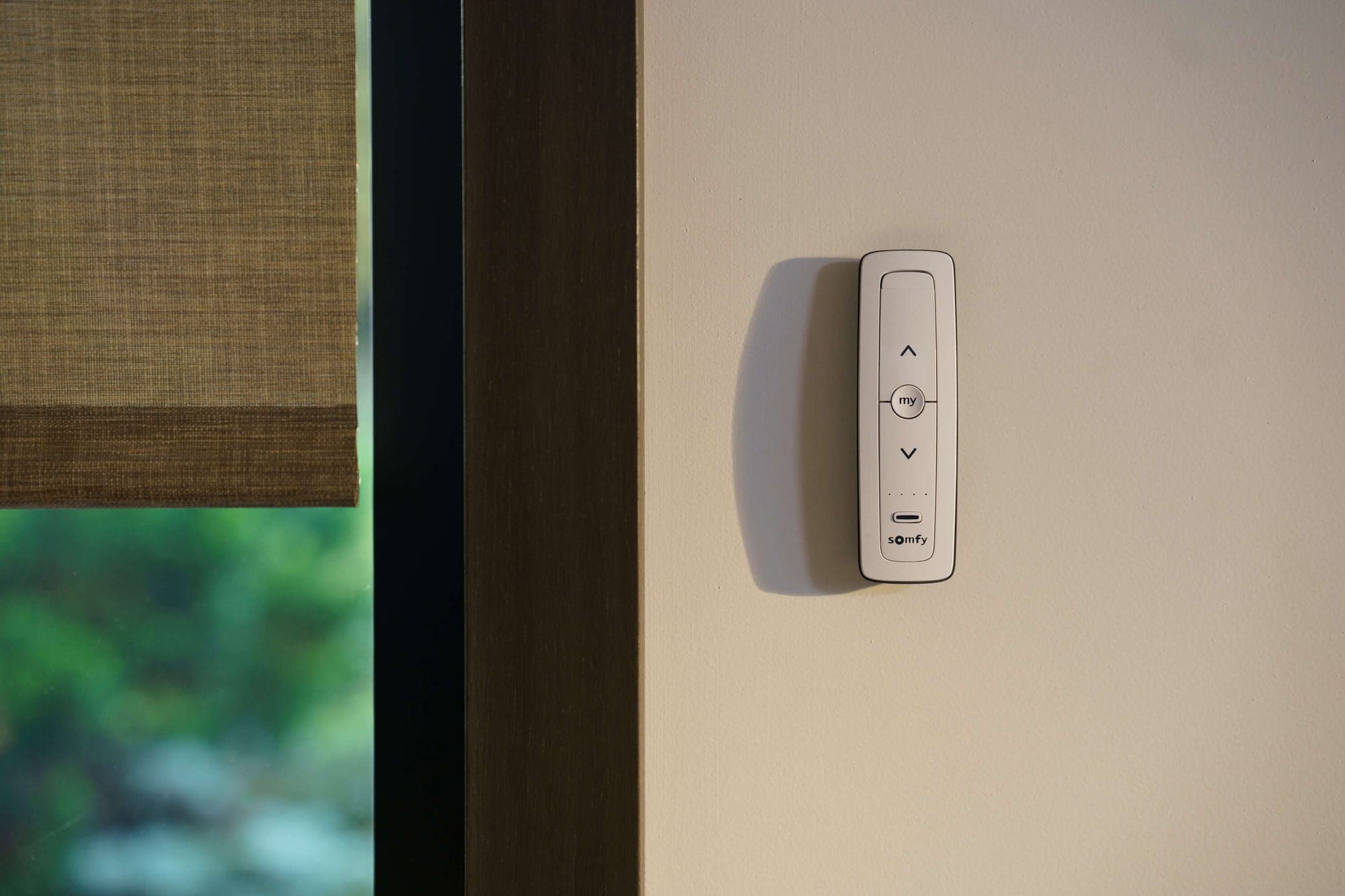 Pilot Somfy Situo 5 w uchwycie ściennym obok okna z roletą